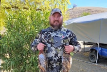 Hunter in full camouflage gear holding two harvested pheasants near a tent at the 2023 Veterans and First Responders Hunt