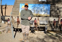 Hunter standing in front of the Pheasants Forever Yolo County chapter sign with harvested pheasants hanging on the bench rack at the 2023 Veterans and First Responders Hunt