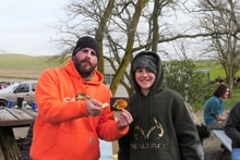 Two hunters — one in blaze orange, one in a camo hoodie — standing together outdoors holding small game birds at the 2023 Youth Mentor Hunt