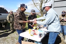 Three men serving themselves food at an outdoor cookout table with condiments and side dishes at the 2024 R3 Upland Bird Hunt post-hunt meal