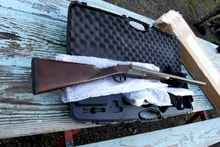 A new shotgun and accessories laid out in an open hard case on a weathered wooden bench at the 2024 Women's Upland Bird Hunt prize table