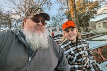 Young girl in a blaze orange vest and camo shirt holding a harvested pheasant in front of a truck at the 2024 Youth Mentor Hunt