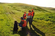 Group of hunters in orange vests gathered in a field with a black Labrador retriever