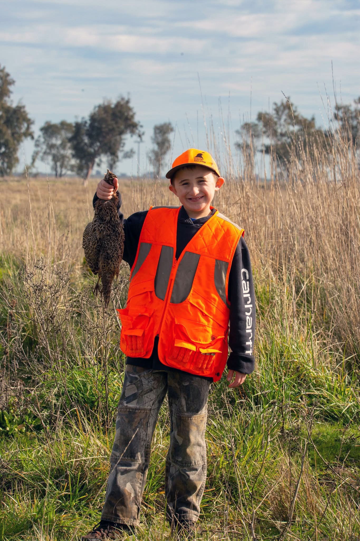Young male hunter holding a harvested pheasant in the field at the 2025 Youth Mentor Hunt