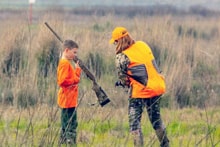 Group of hunters in blaze orange vests walking through a field at the 2025 Youth Mentor Hunt