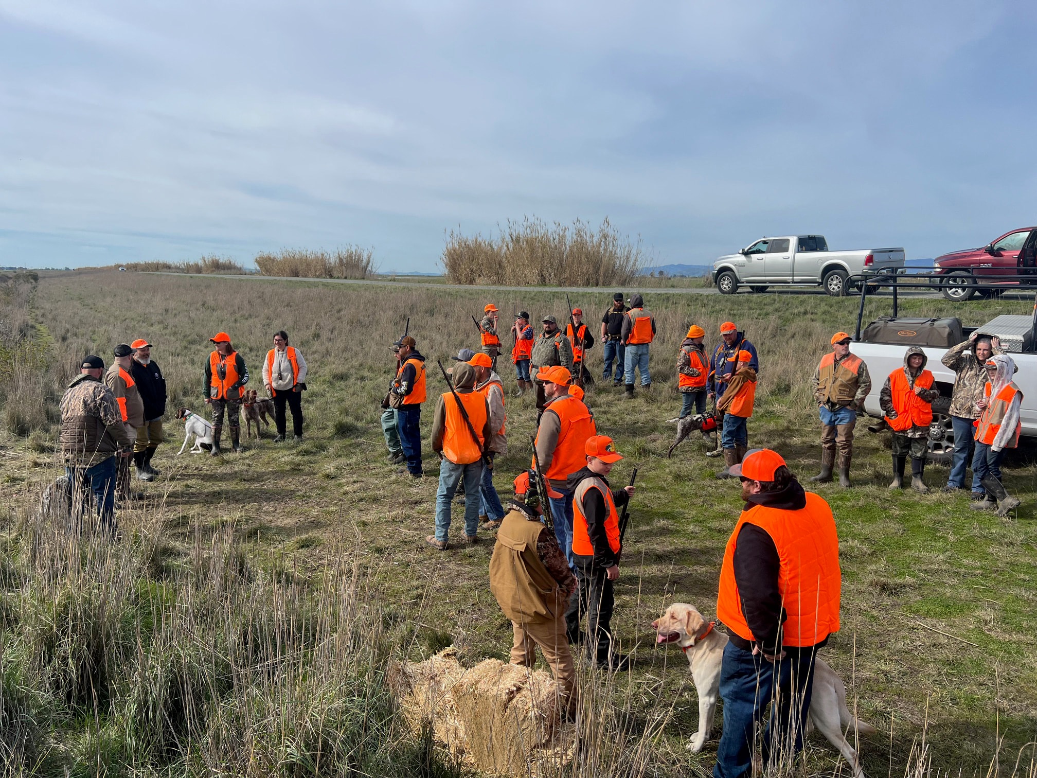 Large group of youth hunters and mentors in blaze orange vests assembled in a grassland field at the 2025 Youth Mentor Hunt