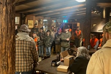 Large crowd of youth hunters and mentors gathered inside a rustic wooden lodge for the pre-hunt briefing at the 2025 Youth Mentor Hunt