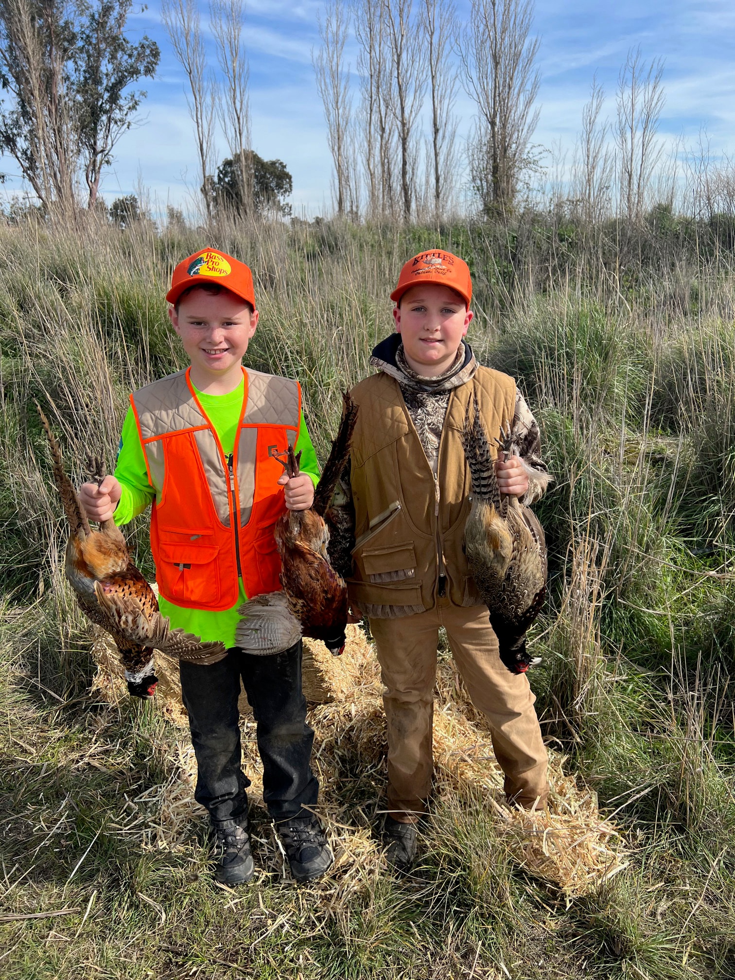 Two young hunters holding harvested game birds in a wetland field at the 2025 Youth Mentor Hunt