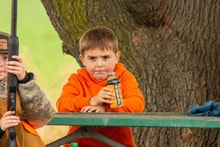 Young boy in an orange jacket leaning against a tree at the 2025 Youth Mentor Hunt